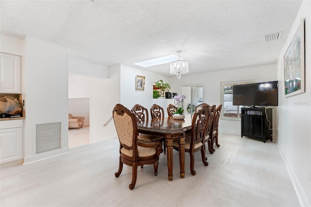 dining space featuring light wood-type flooring, visible vents, a textured ceiling, and an inviting chandelier