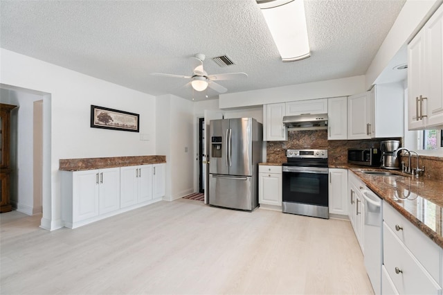 kitchen with under cabinet range hood, a sink, visible vents, appliances with stainless steel finishes, and dark stone countertops