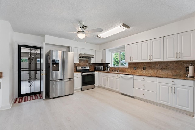 kitchen with stainless steel appliances, white cabinets, light wood-style floors, and under cabinet range hood