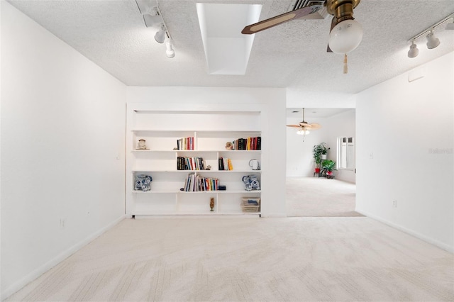 spare room with built in features, rail lighting, a ceiling fan, carpet flooring, and a textured ceiling