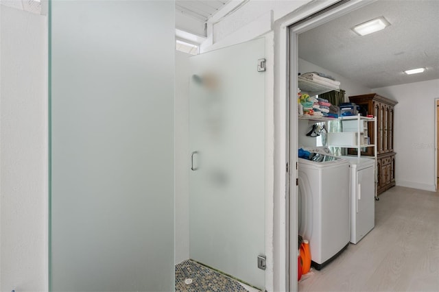 clothes washing area with laundry area, light wood-style flooring, washing machine and clothes dryer, and a textured ceiling