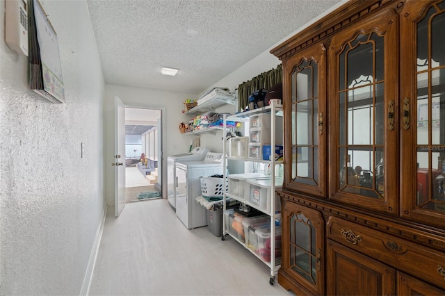 washroom with a textured wall, a textured ceiling, washer and dryer, laundry area, and baseboards