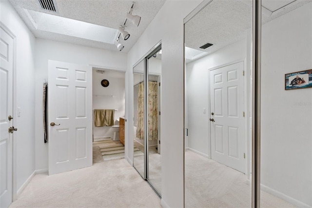 hall with light carpet, rail lighting, visible vents, and a textured ceiling