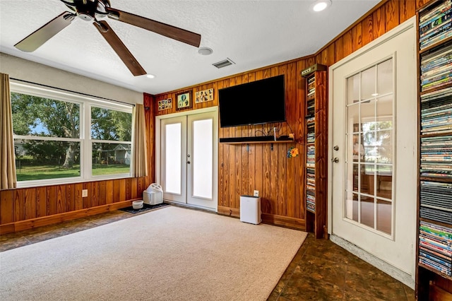 unfurnished living room featuring a textured ceiling, wooden walls, and french doors