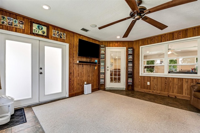 tiled living room featuring wood walls, french doors, ceiling fan, and a textured ceiling