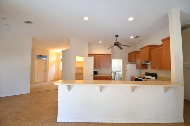 kitchen featuring kitchen peninsula, a kitchen bar, white appliances, ceiling fan, and light tile patterned flooring