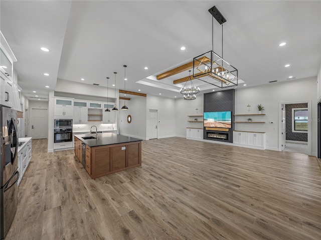 kitchen with a large island with sink, white cabinetry, hanging light fixtures, black oven, and stainless steel microwave