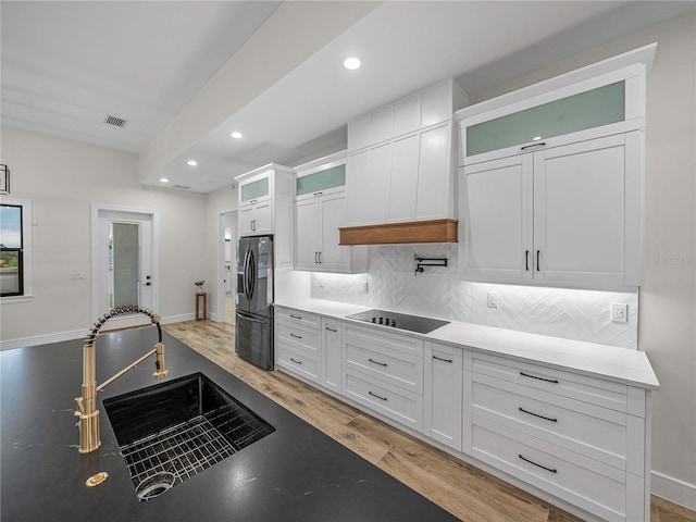 kitchen with stainless steel refrigerator with ice dispenser, light wood-type flooring, black electric stovetop, sink, and white cabinetry