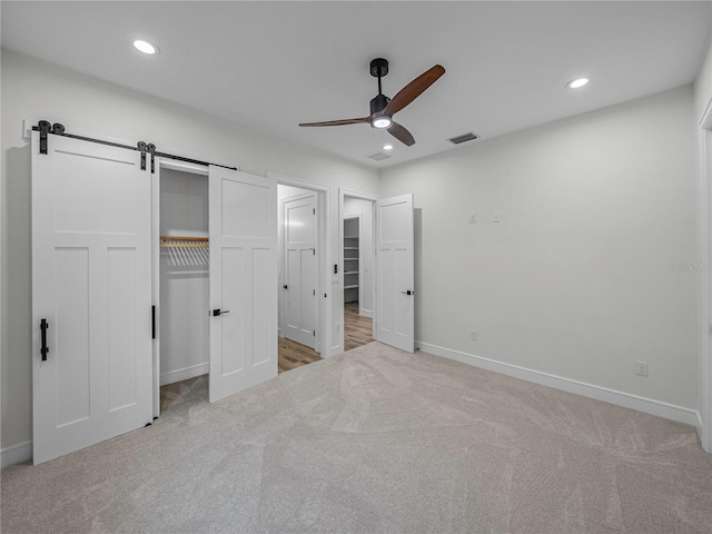 unfurnished bedroom with a barn door, ceiling fan, a closet, and light carpet