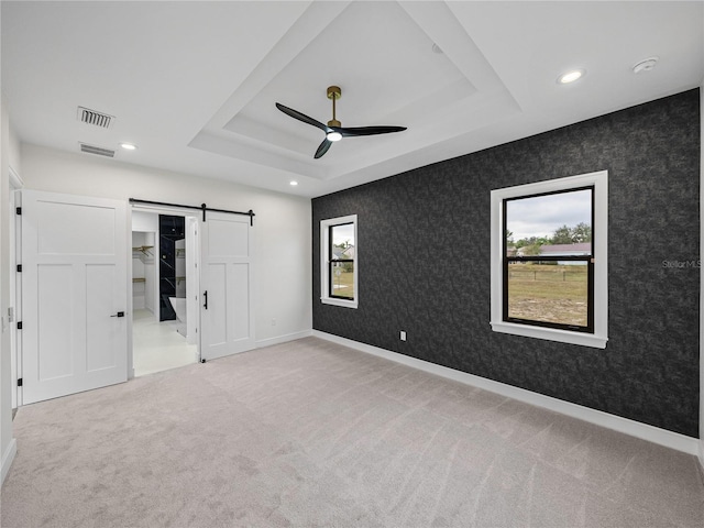 unfurnished bedroom with carpet flooring, ceiling fan, a barn door, and a raised ceiling