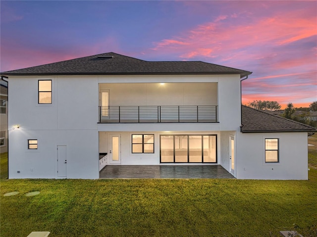 2728 Sunrise Landing Ln, Lakeland, FL 33812 - back of house at dusk with a balcony, a patio area, stucco siding, a lawn, and a shingled roof