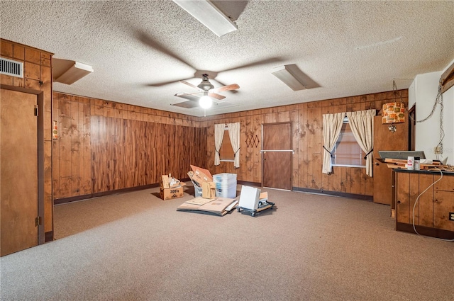 miscellaneous room with a textured ceiling, carpet floors, ceiling fan, and wood walls