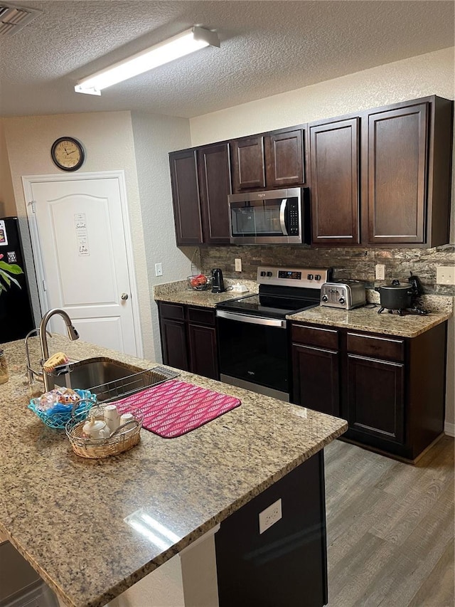 kitchen with backsplash, dark brown cabinetry, hardwood / wood-style flooring, and appliances with stainless steel finishes