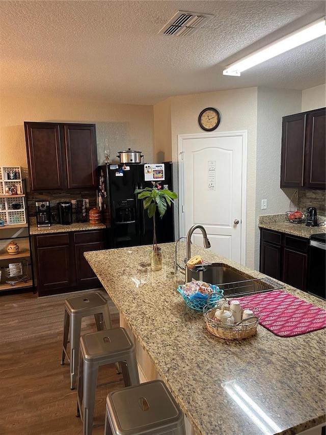 kitchen with sink, black refrigerator with ice dispenser, dark hardwood / wood-style flooring, a textured ceiling, and a kitchen bar