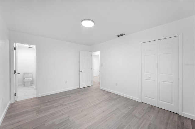 unfurnished bedroom featuring a closet, ensuite bathroom, and light hardwood / wood-style flooring