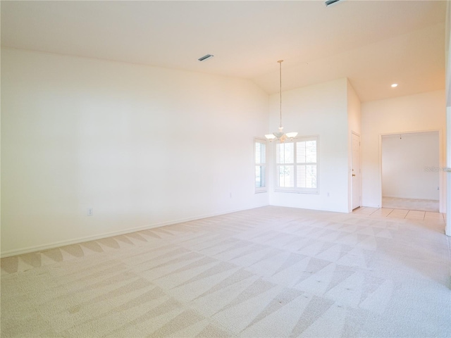 carpeted empty room featuring a notable chandelier and high vaulted ceiling