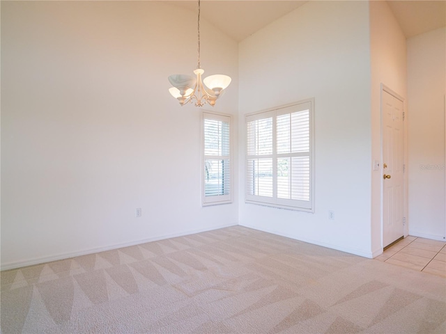 empty room with light colored carpet, high vaulted ceiling, and a notable chandelier