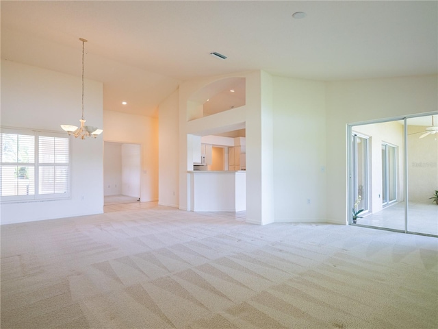 unfurnished living room with ceiling fan with notable chandelier, light carpet, and high vaulted ceiling