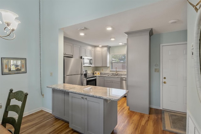 kitchen featuring light stone countertops, sink, kitchen peninsula, appliances with stainless steel finishes, and light wood-type flooring