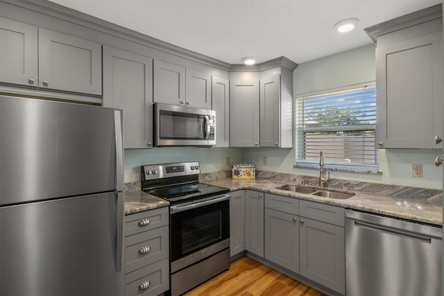 kitchen with light stone counters, gray cabinetry, stainless steel appliances, sink, and light hardwood / wood-style floors