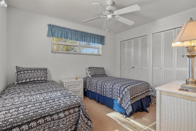 bedroom featuring carpet flooring, ceiling fan, a textured ceiling, and two closets