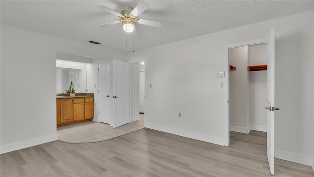 unfurnished bedroom with connected bathroom, ceiling fan, light hardwood / wood-style flooring, and a textured ceiling