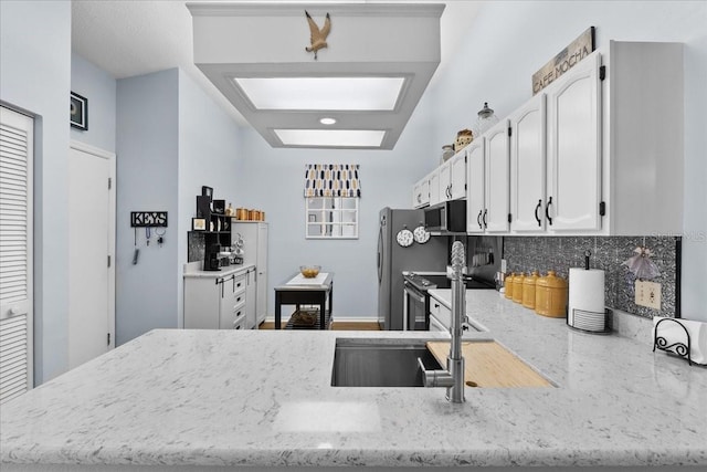 kitchen with white cabinets, backsplash, kitchen peninsula, and light stone countertops