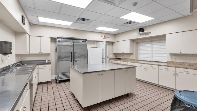 kitchen with a drop ceiling, stainless steel built in refrigerator, sink, a center island, and white cabinetry