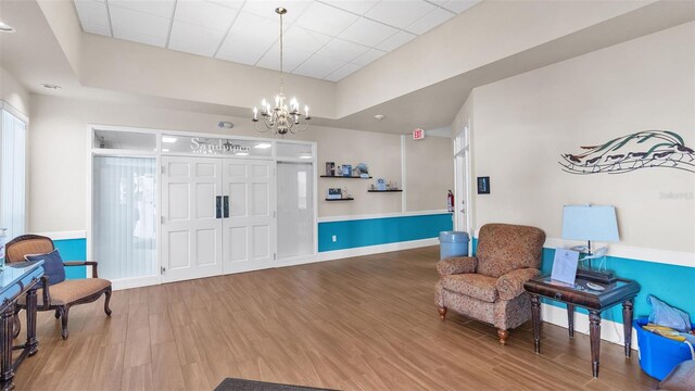 sitting room with hardwood / wood-style floors, a drop ceiling, and an inviting chandelier