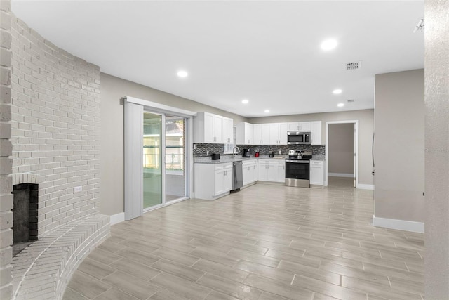 kitchen with backsplash, a fireplace, stainless steel appliances, light hardwood / wood-style flooring, and white cabinets