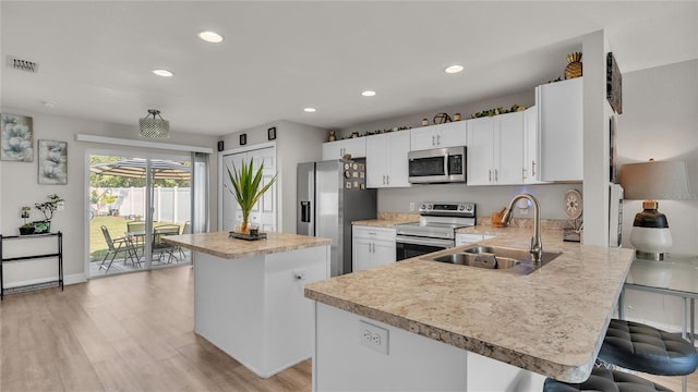 kitchen with appliances with stainless steel finishes, sink, white cabinets, light hardwood / wood-style floors, and a breakfast bar area