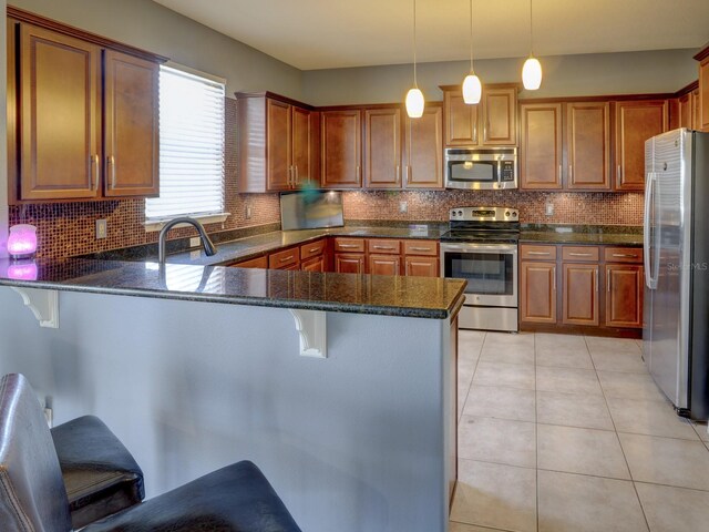 kitchen featuring kitchen peninsula, a kitchen breakfast bar, backsplash, stainless steel appliances, and hanging light fixtures