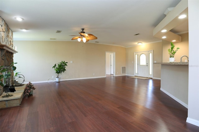 unfurnished living room featuring ornamental molding, dark wood-type flooring, a fireplace, and ceiling fan