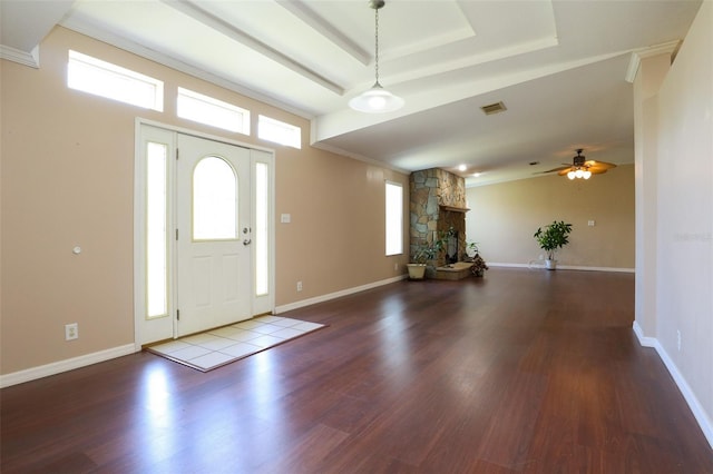 entrance foyer with hardwood / wood-style flooring, ornamental molding, a stone fireplace, and a raised ceiling