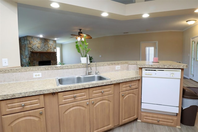 kitchen with a stone fireplace, kitchen peninsula, sink, light hardwood / wood-style floors, and white dishwasher