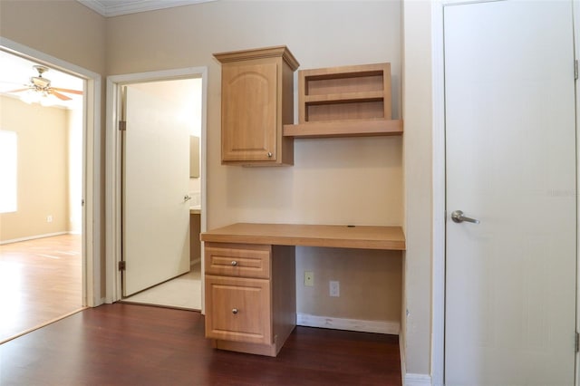 unfurnished office featuring crown molding, built in desk, dark hardwood / wood-style floors, and ceiling fan