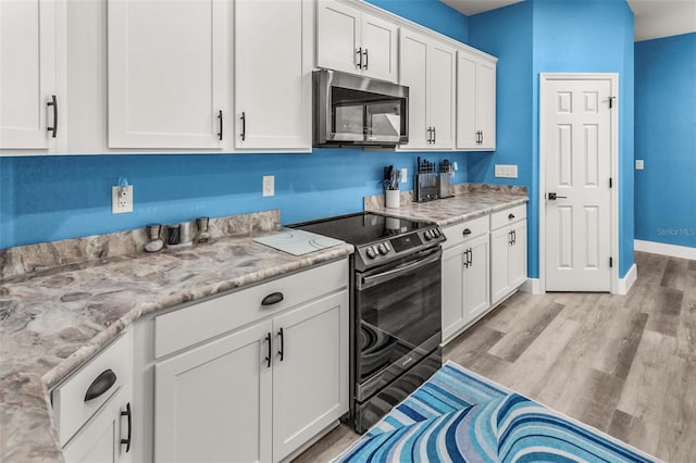 kitchen with stainless steel appliances, light stone countertops, white cabinets, and light hardwood / wood-style flooring