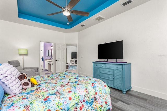 bedroom featuring ceiling fan, a tray ceiling, ensuite bath, and light hardwood / wood-style flooring