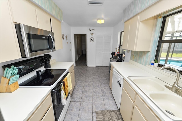 kitchen featuring light tile patterned flooring, cream cabinets, white appliances, and sink