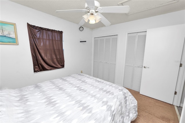 bedroom with a textured ceiling, ceiling fan, light carpet, and two closets