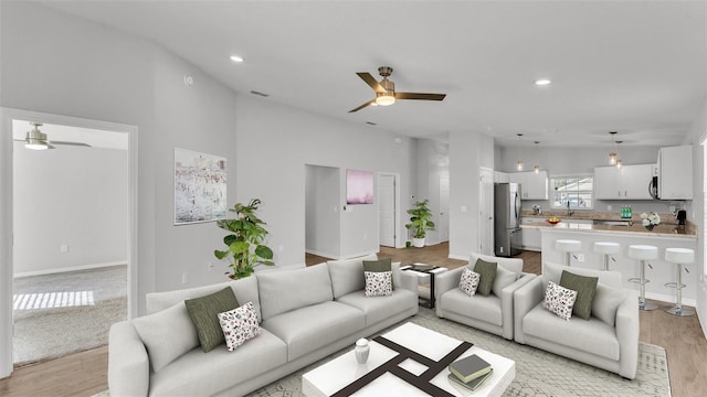 living room with ceiling fan, light hardwood / wood-style floors, and high vaulted ceiling