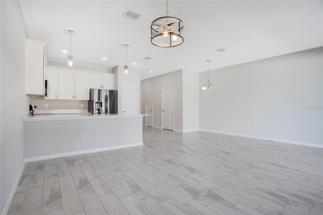 kitchen featuring appliances with stainless steel finishes, light hardwood / wood-style flooring, a notable chandelier, white cabinetry, and hanging light fixtures