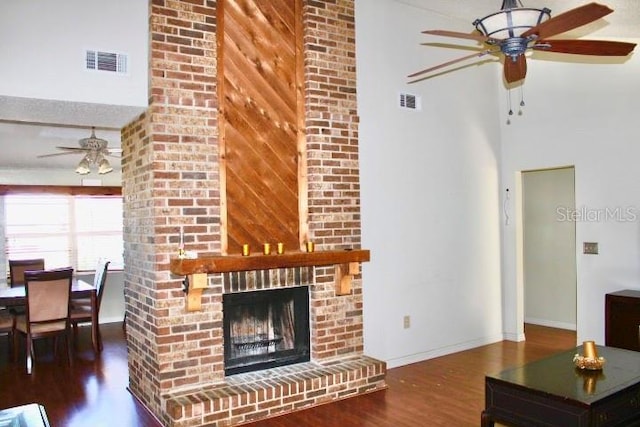 living room with hardwood / wood-style floors, ceiling fan, a towering ceiling, and a brick fireplace