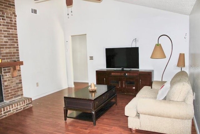 living room with ceiling fan, a fireplace, dark hardwood / wood-style flooring, and a textured ceiling