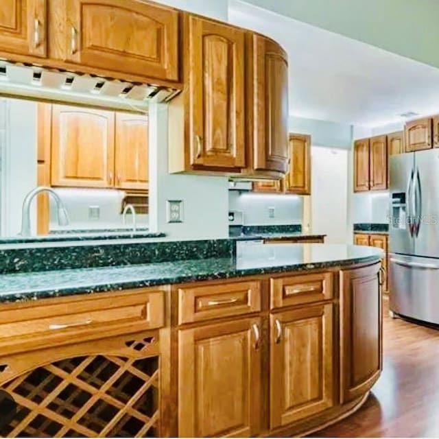 kitchen with stainless steel fridge, dark hardwood / wood-style floors, and dark stone countertops