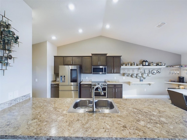 kitchen with lofted ceiling, dark brown cabinetry, sink, appliances with stainless steel finishes, and light stone countertops