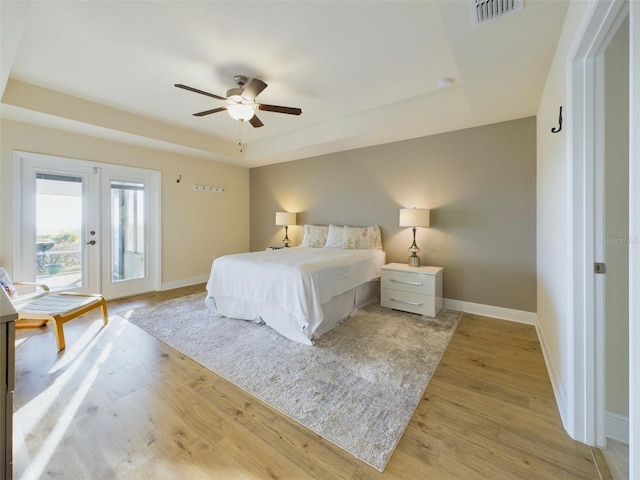 bedroom featuring french doors, a tray ceiling, light hardwood / wood-style floors, and access to exterior