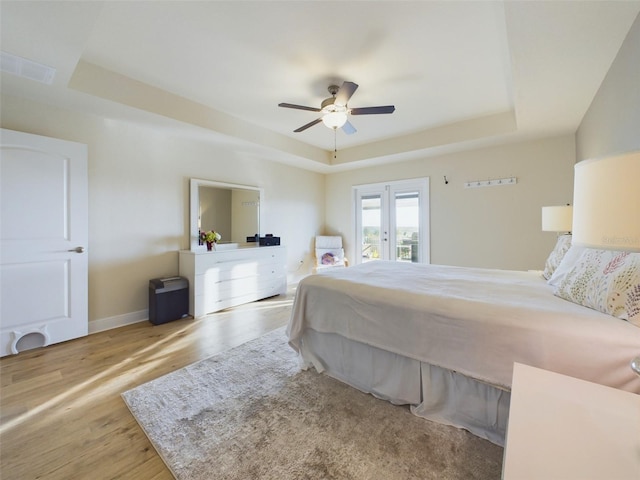 bedroom featuring french doors, a raised ceiling, ceiling fan, and light wood-type flooring