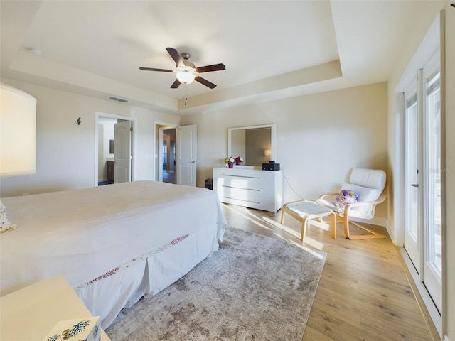 bedroom with a raised ceiling, ceiling fan, multiple windows, and light hardwood / wood-style flooring