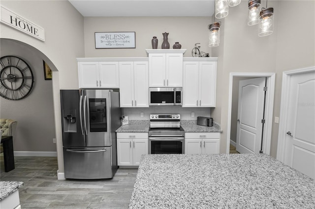 kitchen with light stone counters, light hardwood / wood-style flooring, decorative light fixtures, white cabinets, and appliances with stainless steel finishes